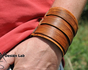 Puede incluir: Un brazalete de cuero marrón con múltiples correas. El brazalete se lleva en la muñeca.