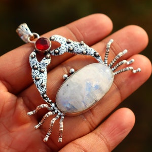 Puede incluir: Colgante de plata en forma de cangrejo con una gran piedra de luna ovalada y un pequeño acento de piedra roja.