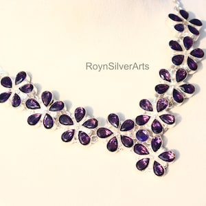 May include: A silver necklace featuring a floral design with purple gemstone petals. The necklace is displayed on a white surface. The text "RoynSilverArts" is visible.