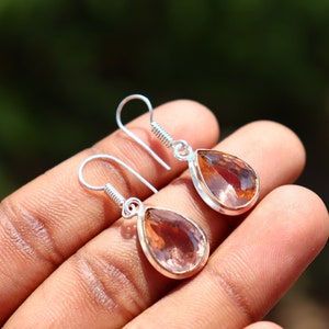 May include: A pair of silver dangle earrings with teardrop-shaped pink and orange gemstones.