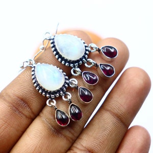 May include: Silver dangle earrings with a pear-shaped moonstone and three dangling red garnet stones.