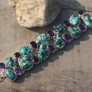 Puede incluir: Un brazalete de plata con piedras turquesa y amatista. El brazalete tiene un cierre de palanca.