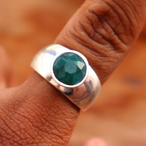 May include: A silver ring with a large, faceted, green emerald gemstone set in a bezel setting.
