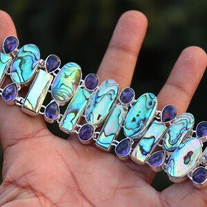 May include: A silver bracelet with iridescent abalone shell and amethyst gemstones. The bracelet has a clasp closure.
