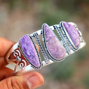 Pode incluir: Um bracelete de prata com três acentos de pedras preciosas roxas e brancas. O bracelete tem um design delicado e adornado.