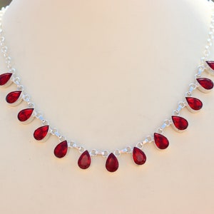 Könnte beinhalten: Eine silberne Halskette mit einer Kette und roten tropfenförmigen Steinen.