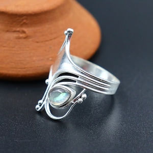 Könnte beinhalten: Ein silberner Ring mit einem filigranen, komplizierten Design, das einen tropfenförmigen, schillernden Labradorit-Edelstein zeigt.