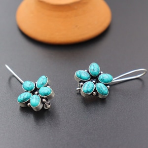 Peut inclure: Une paire de boucles d'oreilles en argent avec des accents de fleurs turquoise. Chaque boucle d'oreille a cinq pierres turquoise serties dans un motif de fleur en argent.