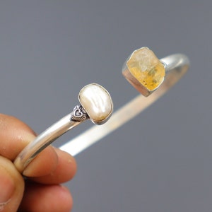 Op de afbeelding: Een zilveren armband met een klein hartje en twee natuurlijke edelstenen. De ene edelsteen is een lichtgele citrien en de andere is een witte parel.