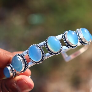 May include: Silver cuff bracelet with oval, pale blue gemstones. The gemstones are set in a decorative silver frame with a twisted rope design. A stylish piece of jewellery.