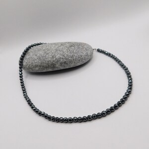 May include: A black hematite beaded necklace with a silver clasp. The necklace is made of small, round beads and is approximately 18 inches long.