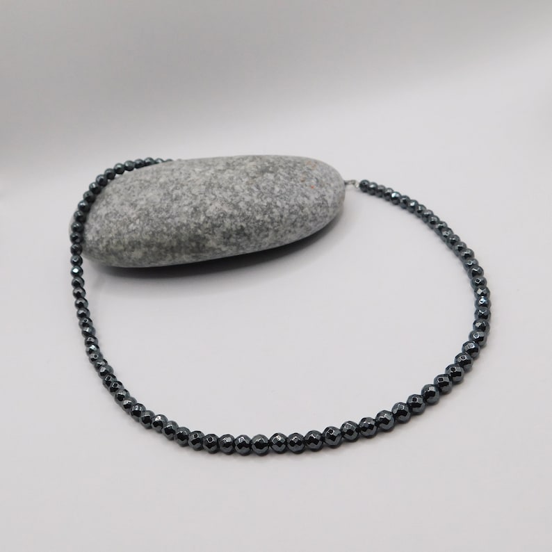 May include: A black hematite beaded necklace with a silver clasp. The necklace is made of small, round beads and is approximately 18 inches long.