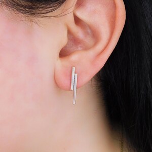 Op de afbeelding: Zilveren oorbellen met drie dunne, verticale staven. De staven zijn op elkaar gestapeld en lichtjes gekanteld.