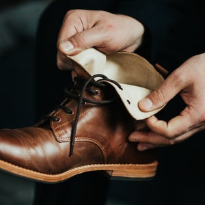 May include: A brown leather boot with a white leather lining. The boot is laced up and has a brown sole.