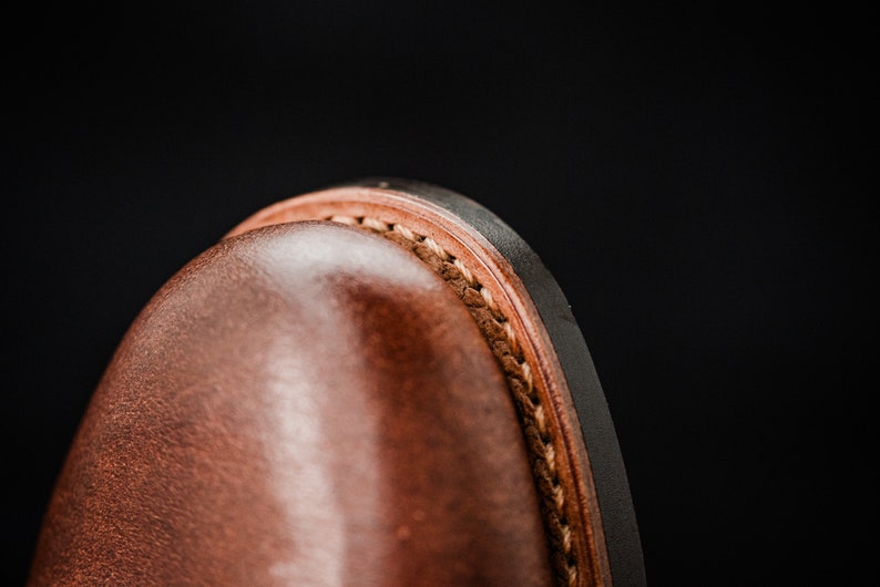 Puede incluir: Primer plano del borde superior de una bota de cuero marr&oacute;n. La bota tiene una suela negra y un detalle de costura marr&oacute;n.