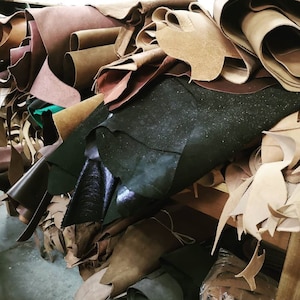 May include: A pile of different colored leather scraps, including brown, black, and tan. The leather is in various shapes and sizes, and some of it is rolled up.