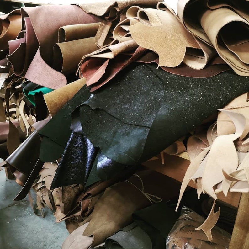 May include: A pile of different colored leather scraps, including brown, black, and tan. The leather is in various shapes and sizes, and some of it is rolled up.