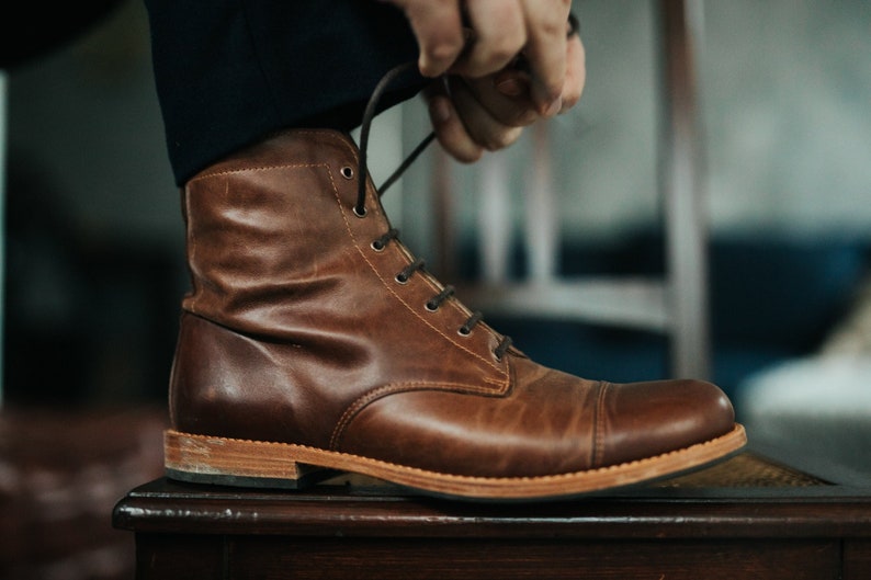 May include: Brown leather lace-up boots with a thick sole. The boots are being tied by a person.