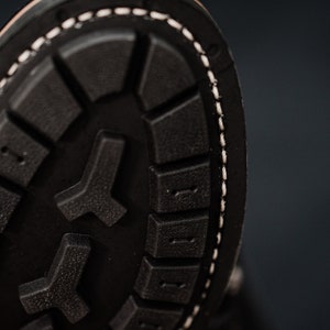 Puede incluir: Primer plano de la suela de un zapato de cuero negro con un borde cosido blanco. La suela tiene un patr&oacute;n texturizado de peque&ntilde;os cuadrados y un dise&ntilde;o en forma de Y m&aacute;s grande.