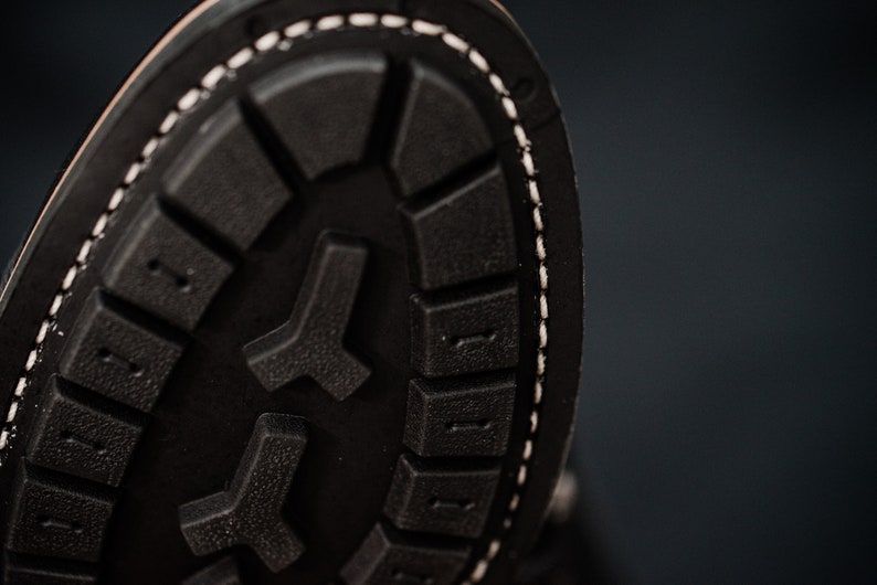Puede incluir: Primer plano de la suela de un zapato de cuero negro con un borde cosido blanco. La suela tiene un patr&oacute;n texturizado de peque&ntilde;os cuadrados y un dise&ntilde;o en forma de Y m&aacute;s grande.