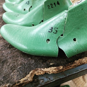 May include: Close-up of green shoe lasts with the numbers "35" and "2214" written on them. The lasts are on a wooden surface.