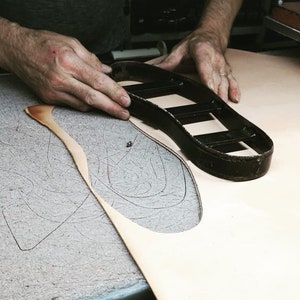May include: A leather shoe sole being cut out using a metal template. The template is placed on top of a piece of leather and the excess leather is cut away.
