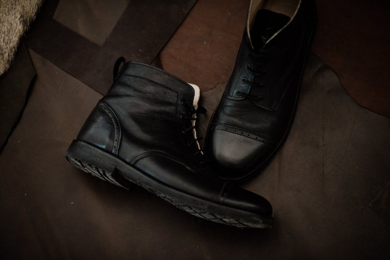 May include: Two pairs of black leather boots with laces. One boot is a lace-up ankle boot with a rounded toe. The other boot is a low-top boot with a cap toe.