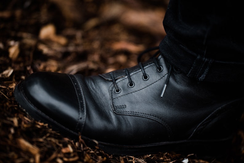 May include: Close-up of a black leather boot with laces and a cap toe. The boot is worn and has a distressed look.