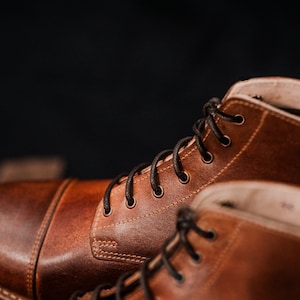 Puede incluir: Primer plano de dos botas de cuero marr&oacute;n con cordones negros. Las botas tienen un estilo cl&aacute;sico y est&aacute;n hechas de cuero de alta calidad.