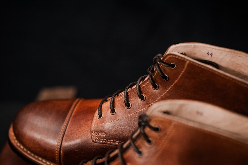 Puede incluir: Primer plano de dos botas de cuero marr&oacute;n con cordones negros. Las botas tienen un estilo cl&aacute;sico y est&aacute;n hechas de cuero de alta calidad.