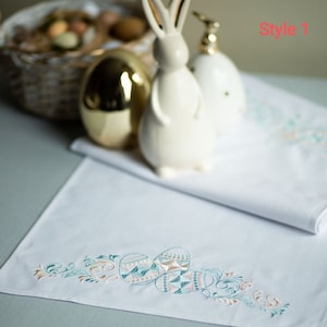 Op de afbeelding: Witte geborduurde tafelloper met een ontwerp van gestileerde eieren en bloemmotieven in tinten teal, bruin en crème. De tekst "Style 1" is zichtbaar in de rechterbovenhoek van de afbeelding.