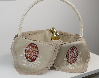 May include: A white wicker basket with a beige fabric liner and embroidered Easter eggs. The basket has a white handle and is decorated with lace trim.