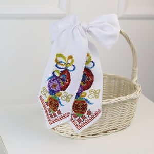 May include: White wicker basket with a white fabric bow decorated with colourful beaded embroidery. The embroidery features a floral design with red, yellow, blue, and green beads.
