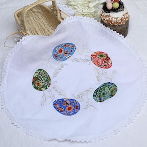 May include: White round tablecloth with a lace trim and embroidered colourful Easter eggs.