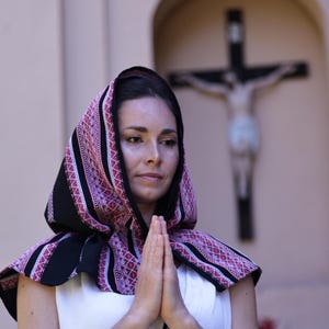 May include: A head covering featuring a black base with intricate red and white geometric embroidery patterns. The fabric drapes over the head and shoulders, showcasing a detailed woven design with repeating diamond and linear motifs throughout.
