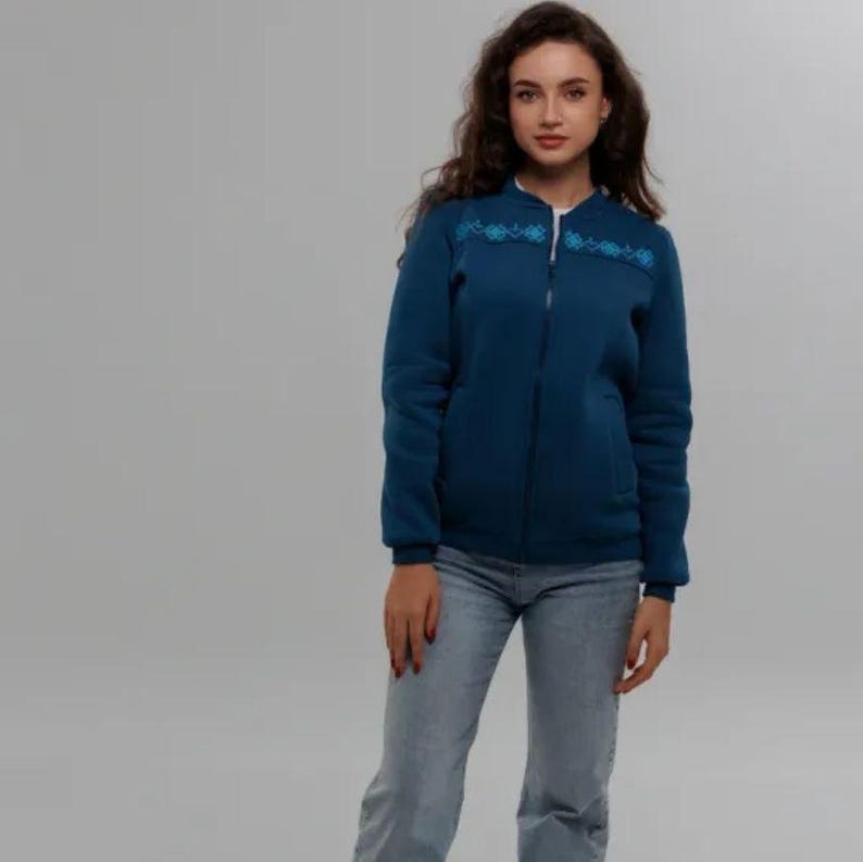 Puede incluir: Una chaqueta azul oscuro con cremallera con un dise&ntilde;o bordado azul en el pecho. La chaqueta est&aacute; hecha de un material suave y c&oacute;modo y tiene un corte holgado.