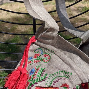 May include: A beige linen tote bag with red tassels and colorful embroidered floral designs.