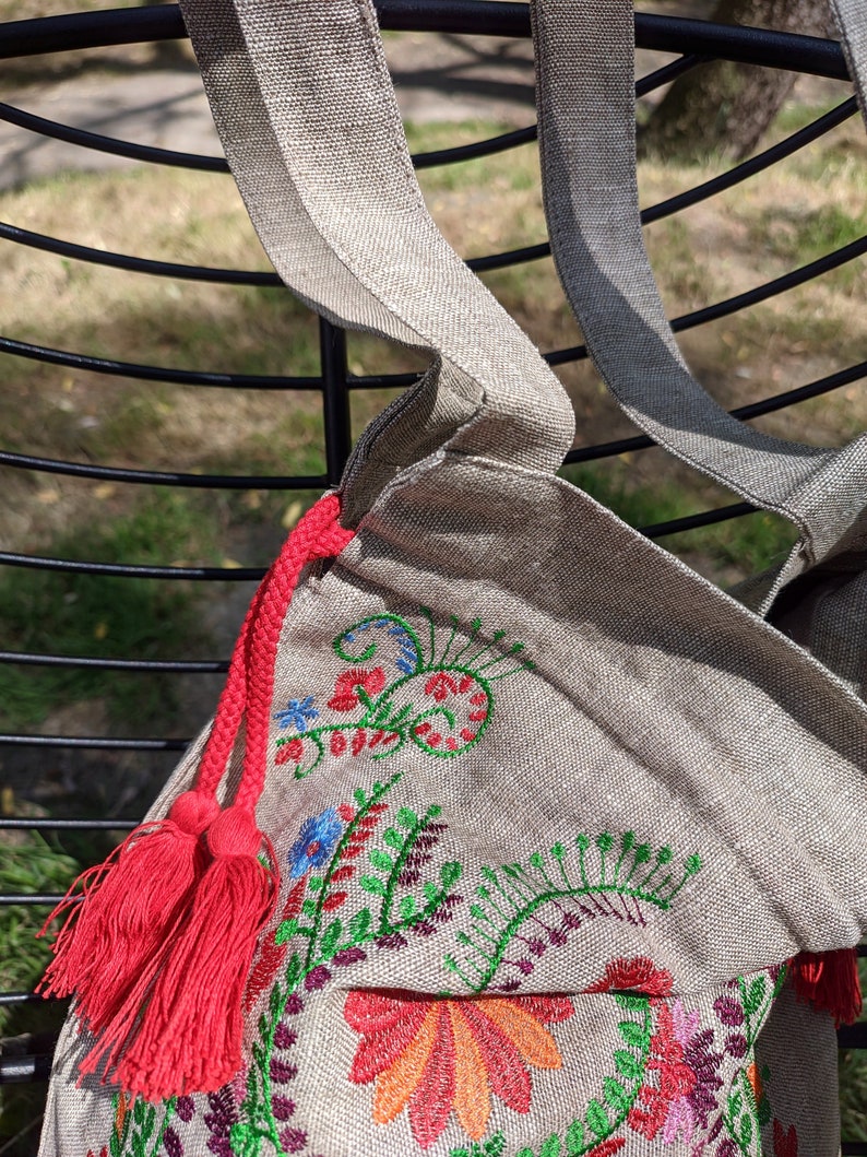 May include: A beige linen tote bag with red tassels and colorful embroidered floral designs.