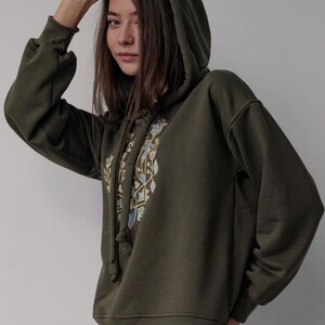 May include: A dark green hooded sweatshirt with a geometric design in blue, yellow, and brown on the front. The hoodie has a drawstring.