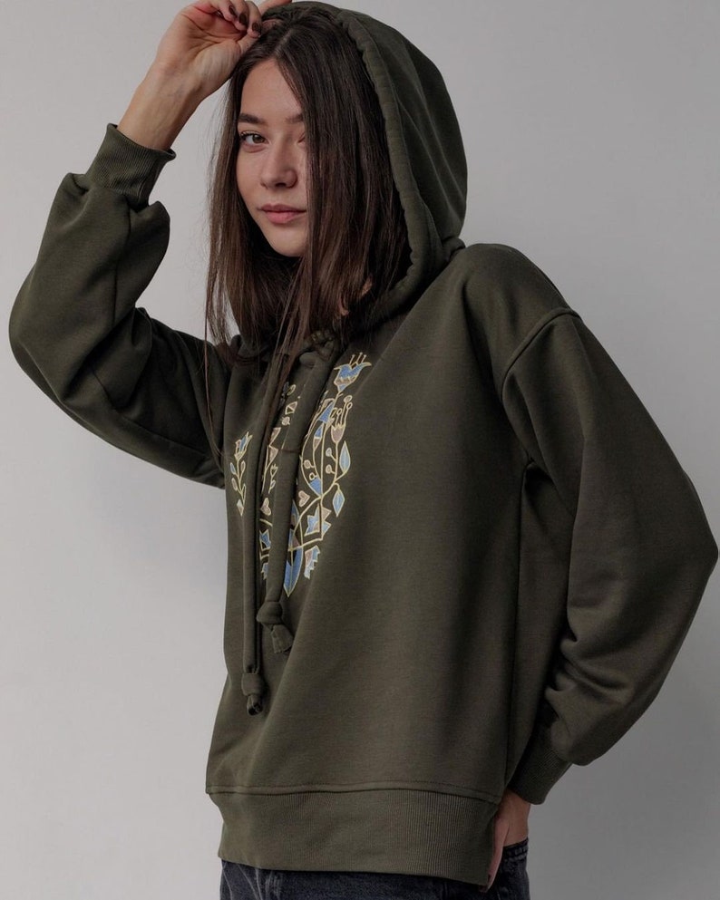 May include: A dark green hooded sweatshirt with a geometric design in blue, yellow, and brown on the front. The hoodie has a drawstring.
