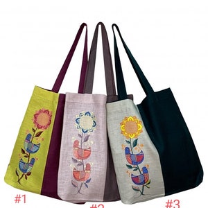 Puede incluir: Cuatro bolsas de mano con dise&ntilde;os florales y de p&aacute;jaros bordados. Las bolsas tienen paneles de diferentes colores, incluyendo verde, morado y gris. Cada bolsa presenta una correa larga y un patr&oacute;n bordado &uacute;nico. Las bolsas est&aacute;n numeradas.