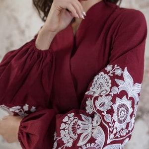 K&ouml;nnte beinhalten: Eine lang&auml;rmelige Bluse in Rotbraun mit wei&szlig;en, gestickten Blumenmustern an den &Auml;rmeln.