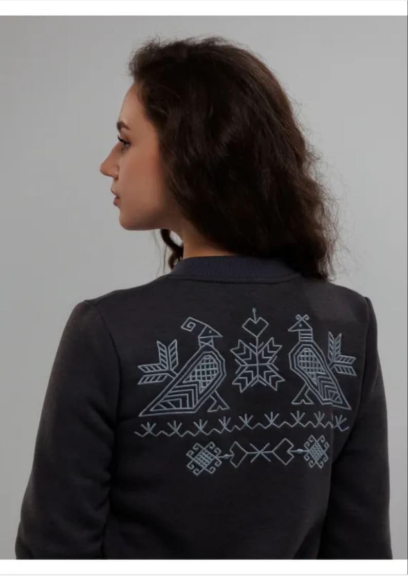 Puede incluir: Una sudadera gris oscuro con un dise&ntilde;o bordado blanco en la espalda. El dise&ntilde;o presenta dos p&aacute;jaros estilizados y un copo de nieve.
