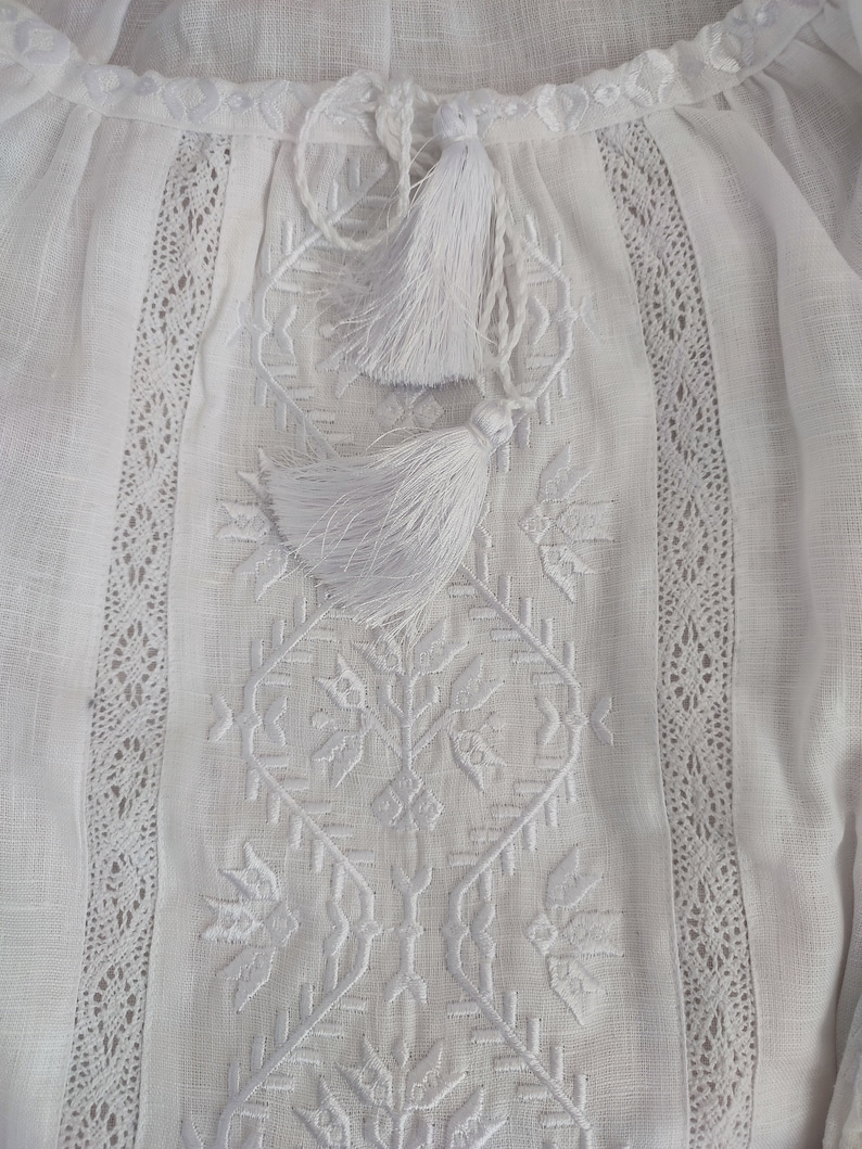 Peut inclure: Chemise en lin blanc avec broderie blanche et bordure en dentelle. La chemise a un lien &agrave; glands blanc au niveau du col.