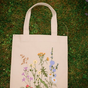 Beige canvas tote bag with botanical embroidery.