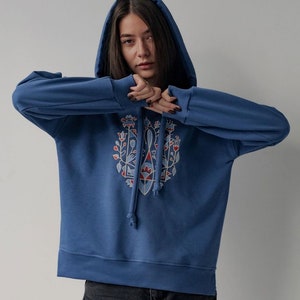 May include: A blue hooded sweatshirt with a colorful floral design on the front. The design features a geometric pattern with red, blue, and white accents.