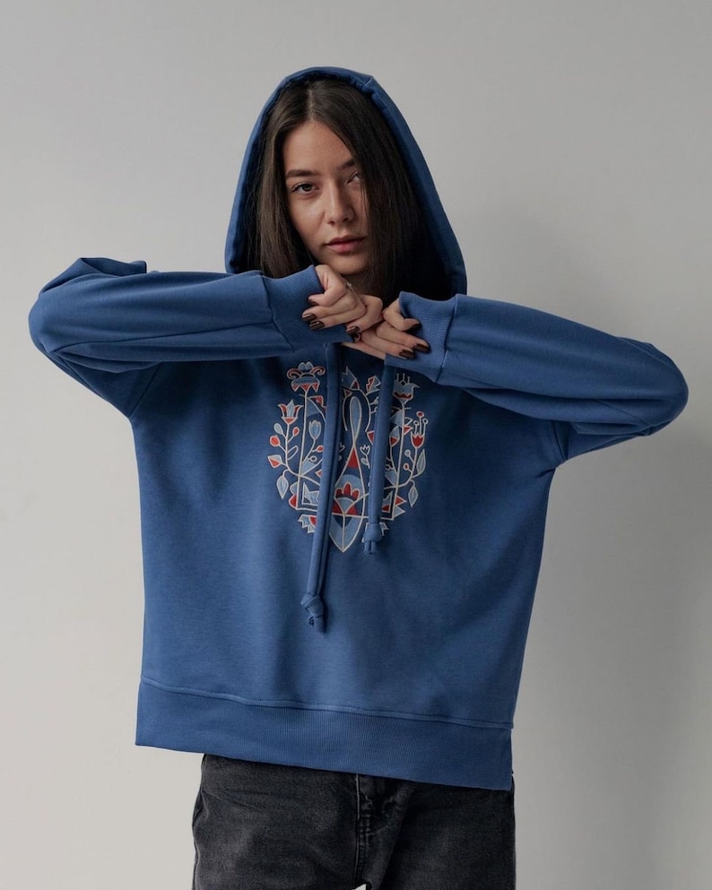 May include: A blue hooded sweatshirt with a colorful floral design on the front. The design features a geometric pattern with red, blue, and white accents.