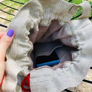 May include: A beige linen drawstring bag with a blue phone inside. The bag has a brown lining and a red drawstring.