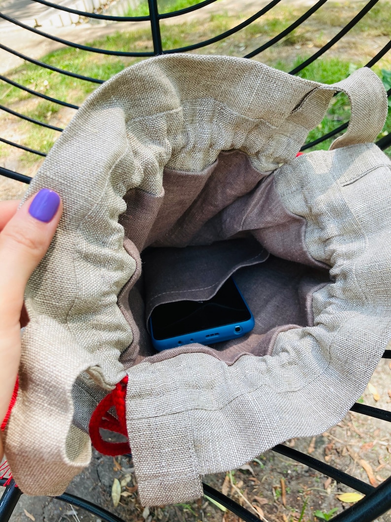 May include: A beige linen drawstring bag with a blue phone inside. The bag has a brown lining and a red drawstring.