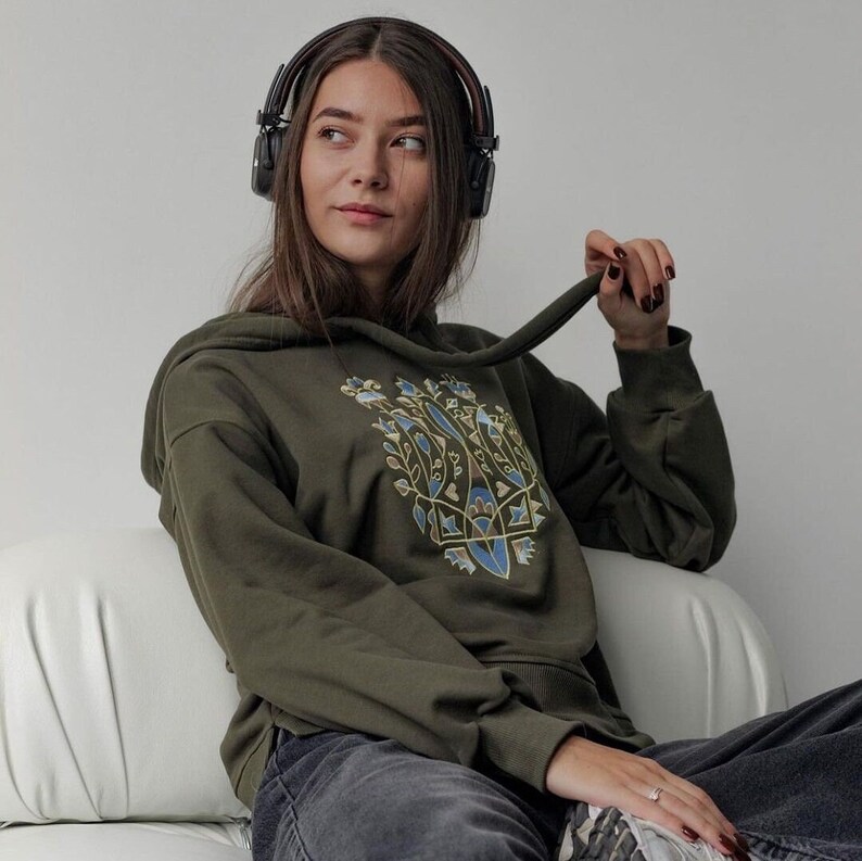 May include: A woman wearing a green hooded sweatshirt with a geometric design on the front. She is wearing headphones and looking to the right.